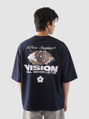 Close-up back view of a male model wearing the navy "Never Stopping Culture" t-shirt, featuring a bold eye graphic and the phrase “VISION WILL NEVER LET US” in puff and screen print – symbolizing unwavering drive and hustle.