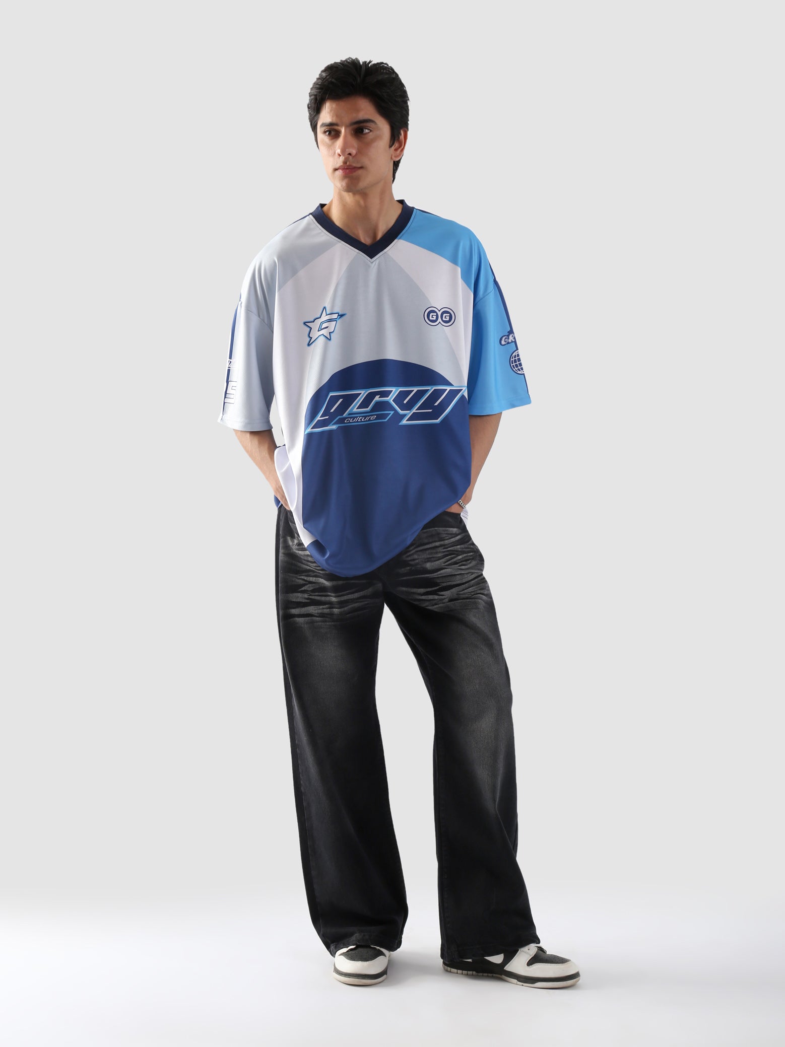 Full body view of man wearing oversized blue and white racing jersey with black baggy jeans and sneakers – Groovy Culture streetwear look Pakistan

