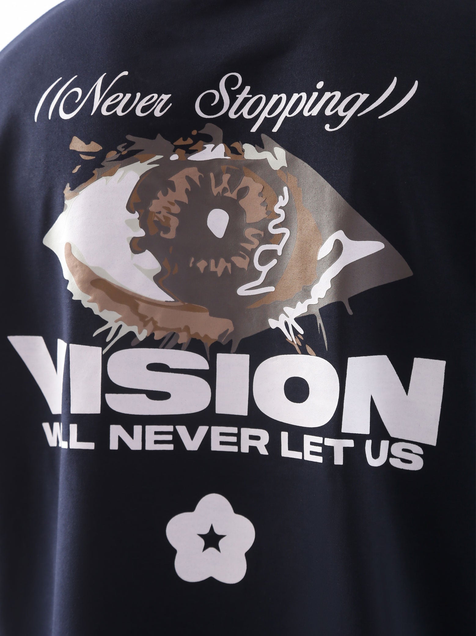 Close-up of the back graphic on the "Never Stopping Culture" t-shirt in navy blue, featuring a bold eye illustration and the text “VISION WILL NEVER LET US” in a mix of puff and screen print, representing unshakeable focus and grind culture.
