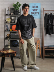 Male model wearing black oversized GRVY t-shirt with splatter-print detail, styled with cream cargo pants in a modern streetwear setup.