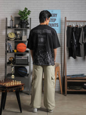 Full back shot of black graphic tee with text “Groovy Effect” and “Love Over Fear,” styled by male model in lifestyle backdrop.