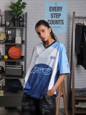 Woman wearing oversized blue and white racing jersey with bold graphics – Groovy Culture unisex streetwear shot in lifestyle indoor setup Pakistan
