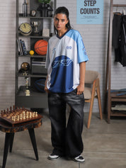 Full body view of woman in oversized blue and white racing jersey and black baggy jeans – Groovy Culture unisex streetwear shot in indoor lifestyle scene Pakistan

