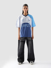 Full body view of woman in oversized blue and white racing jersey and black baggy jeans – Groovy Culture unisex streetwear shot in indoor lifestyle scene Pakistan
