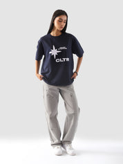 Full-body view of a model wearing the "Never Stopping Culture" tee in navy blue. The oversized fit and front graphic featuring a bold star and "CLTR" text evoke a strong streetwear identity rooted in hustle and ambition.