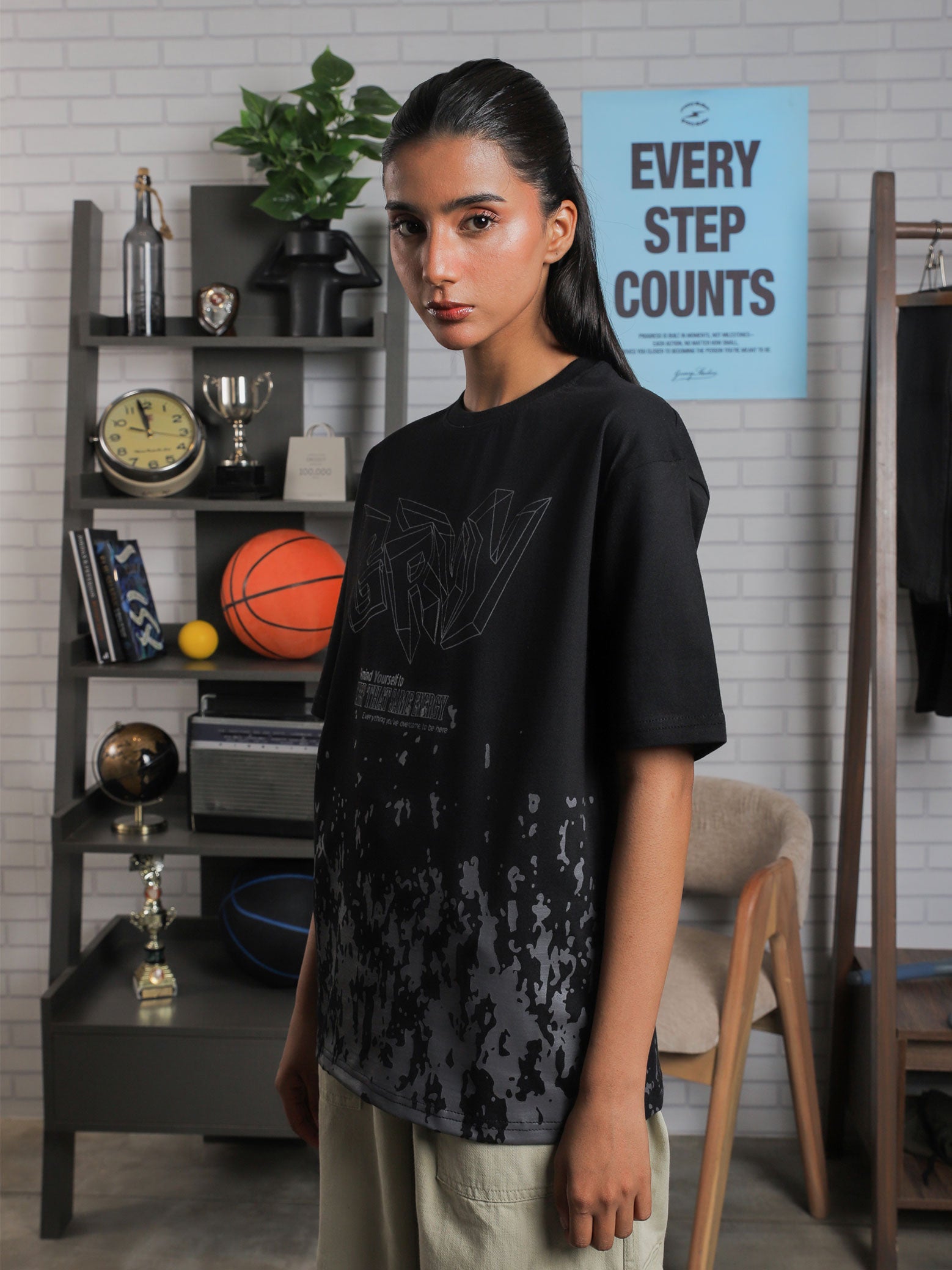 Female model in monotone streetwear, styling the “GRVY” graphic tee in black with an abstract paint-splatter design near hem.