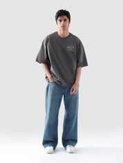 Male model wearing stone grey oversized t-shirt in Pakistan by Groovy – drop shoulder, baggy fit graphic tee styled with loose denim jeans