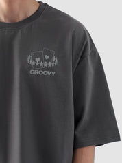 Male model wearing stone grey oversized t-shirt in Pakistan by Groovy – drop shoulder, baggy fit graphic tee styled with loose denim jeans